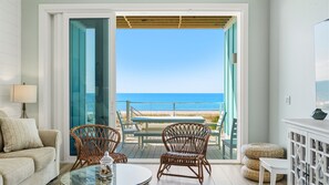 Ein Zimmer mit Blick auf den Strand, einem Glastisch, Korbstühlen, einer Couch und einem Schrank.
