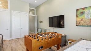 Ein Zimmer mit einem Kicker, einem an der Wand befestigten Fernseher und einer Tür zu einem anderen Raum.