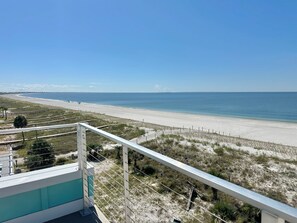 Une vue sur la plage depuis un balcon doté d’une balustrade, avec une plage de sable et l’océan en toile de fond.