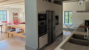 Una cocina moderna con horno empotrado, refrigerador y lavaplatos. Hay un comedor con mesa y sillas, y un ventanal que proporciona luz natural.