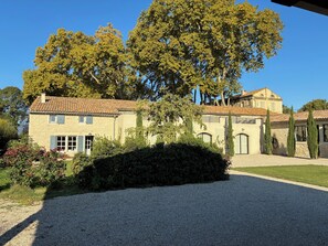 A stone building with a tiled roof, surrounded by greenery and a gravel driveway. - Drôme Provençale Detached house in 18th century property, tennis access (Pierrelatte)