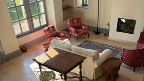 Un salón espacioso con un ventanal grande, una mesa de madera, un sofá blanco y un sillón rojo estampado.