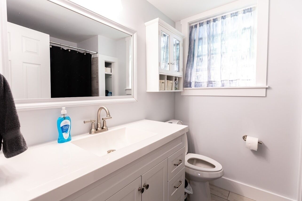 Een badkamer met een wit wastafel, een spiegel, een toilet en een raam met gordijnen.