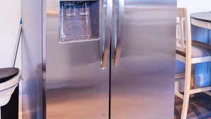 A stainless steel refrigerator with a water dispenser, located in a room with a wooden dining table and chairs.