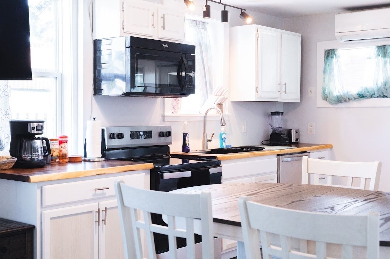 A modern kitchen with white cabinets, a black microwave, a stove, and a coffee maker.