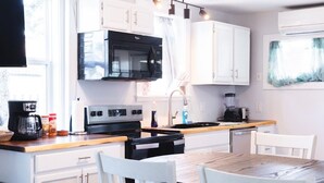 A modern kitchen with white cabinets, a black microwave, a stove, and a coffee maker.