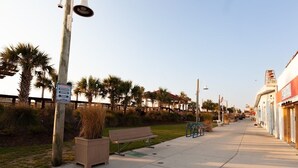 A coastal walkway with benches, palm trees, and a clear sky.