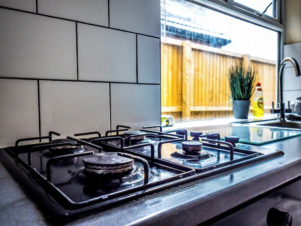 Una cocina con estufa a gas, una ventana y un cerco de madera en el exterior.