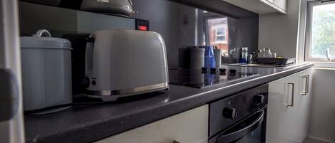 A kitchen with a toaster, kettle, and coffee maker on the counter, a stove, oven, and cabinets.