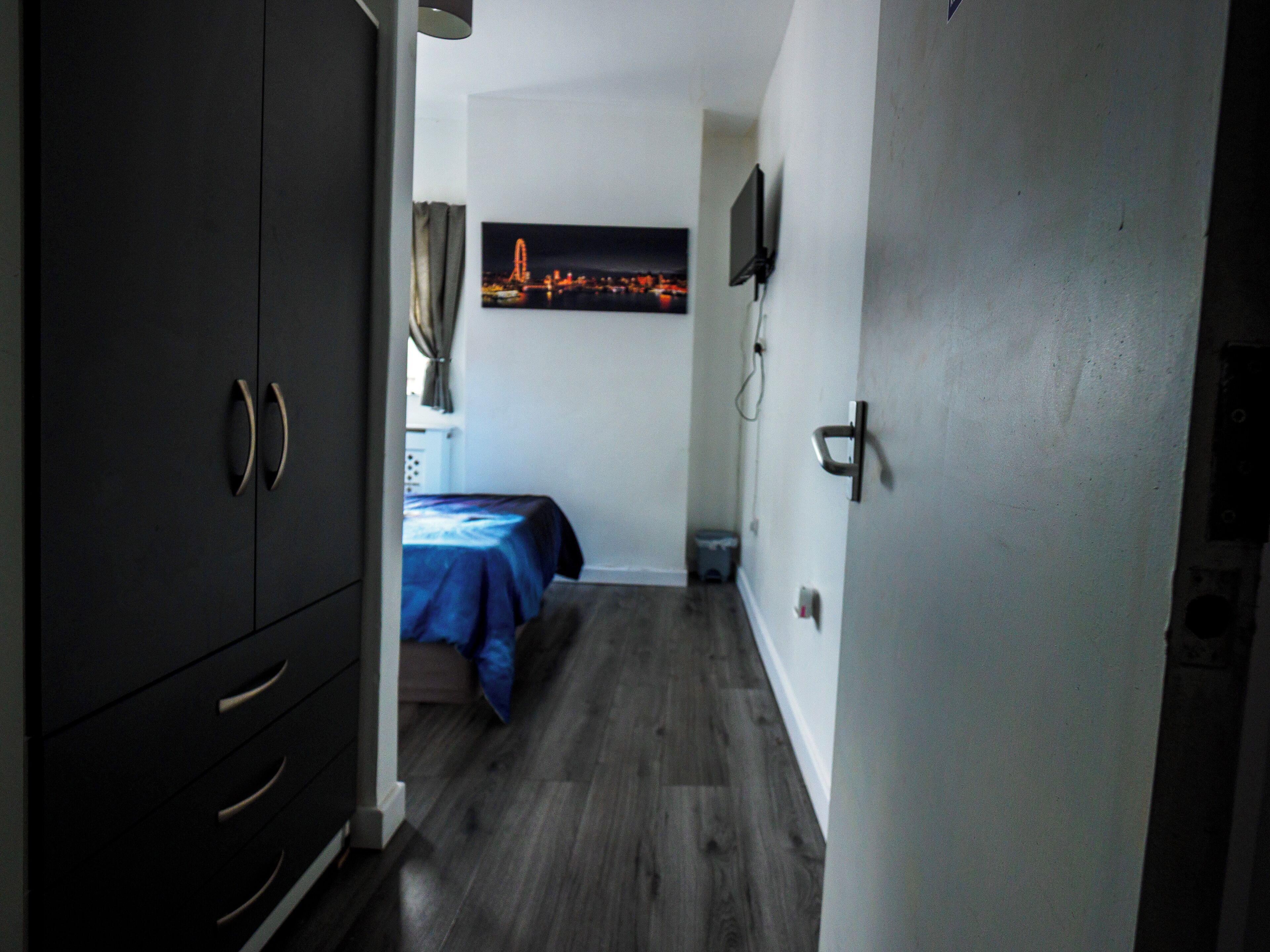 A narrow hallway leading to a bedroom with a bed, a wardrobe, and a TV mounted on the wall.