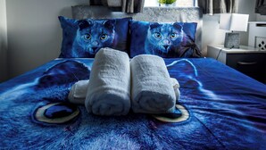Une chambre d’hôtel avec un lit agrémenté d’une couverture et de coussins aux motifs bleus, une table de chevet avec une lampe et une fenêtre avec des rideaux.