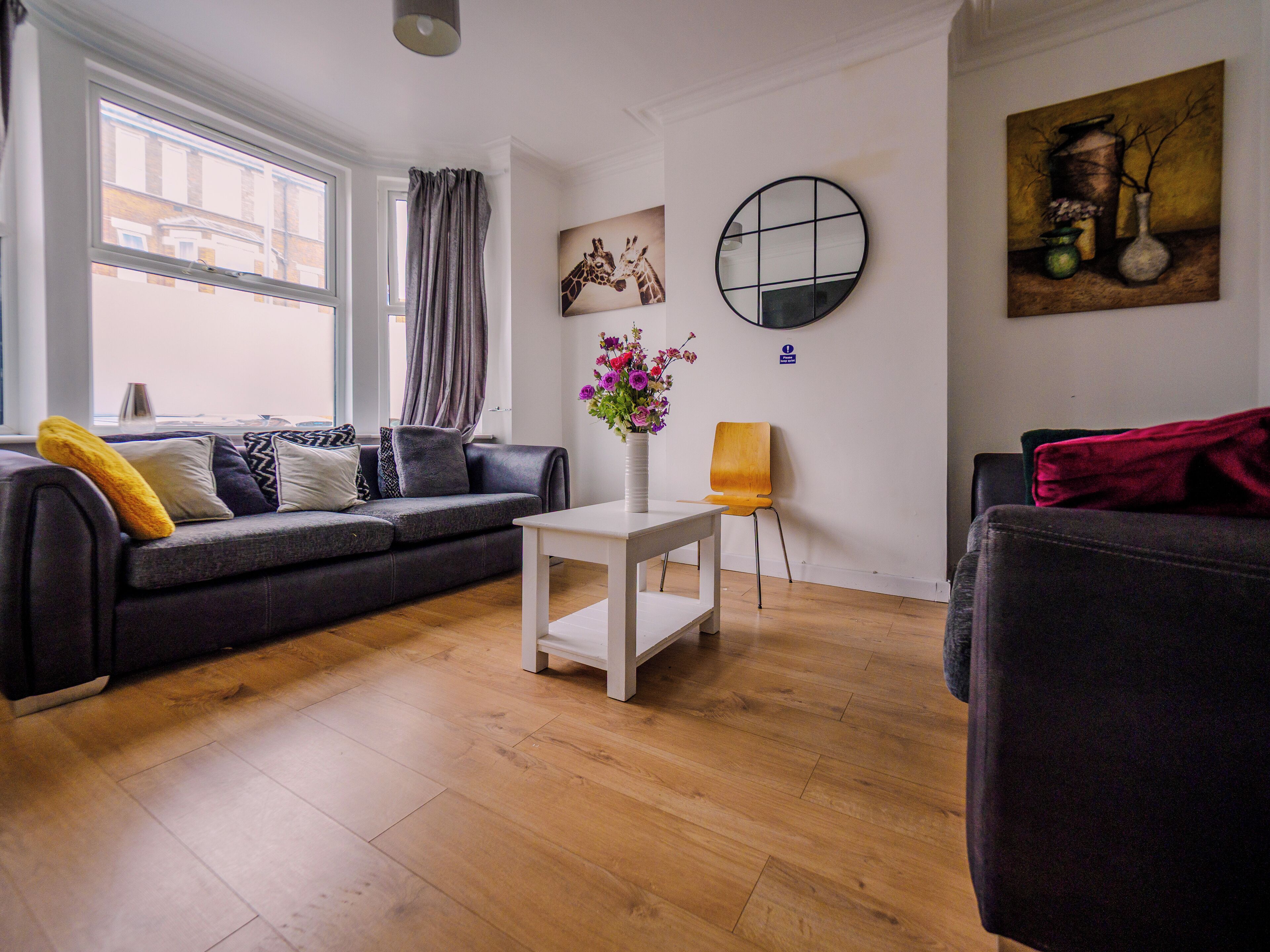 Una sala moderna con un sofá gris, una mesa de centro blanca y piso de madera.