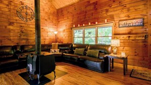 Interior acogedor de una cabaña con chimenea, sofá de cuero y ventana con vistas a la vegetación.
