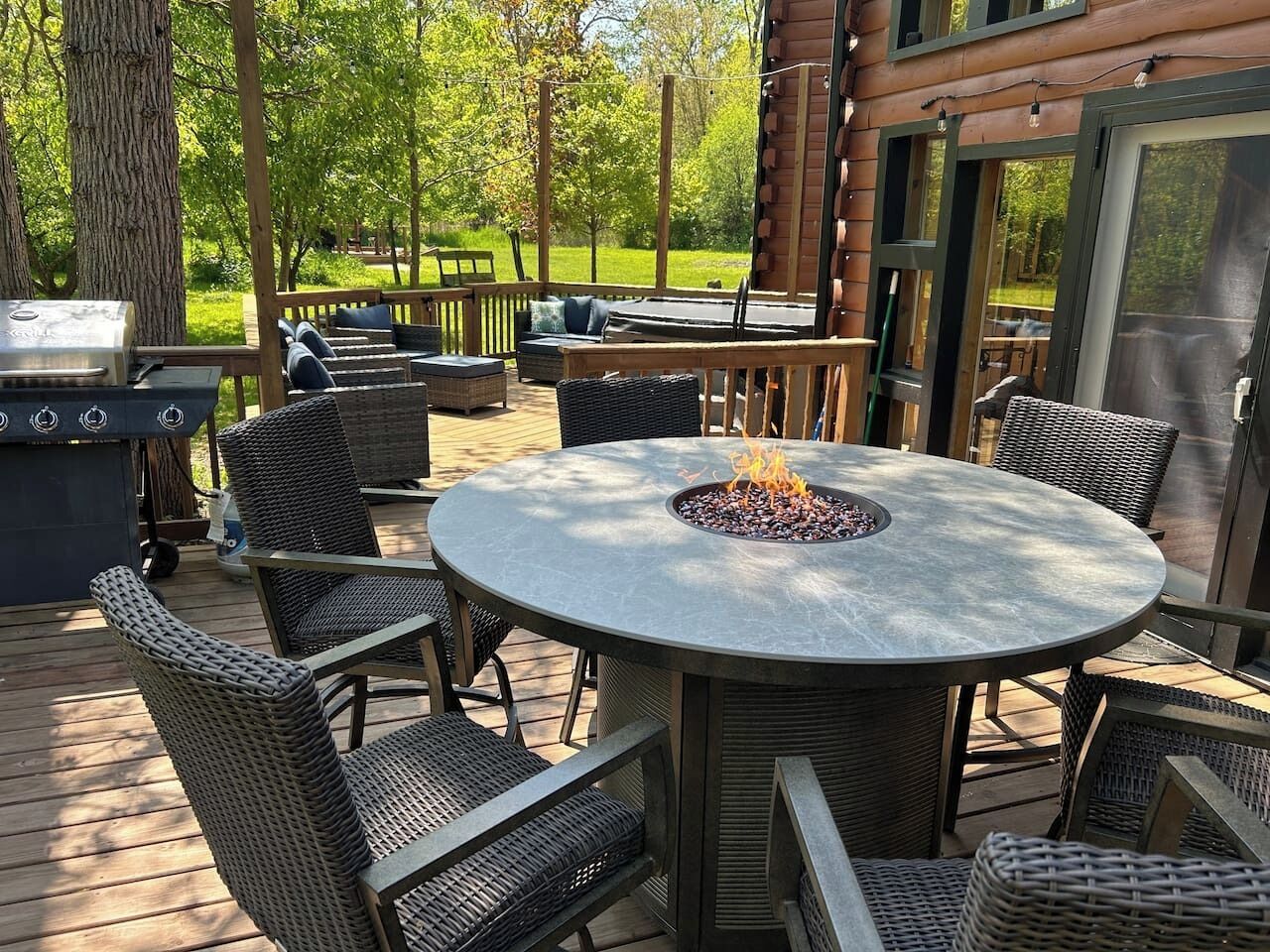 A deck with a round table, wicker chairs, and a fire pit.