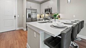 A modern kitchen with white cabinetry, stainless steel appliances, and a central island with seating. - Elegant King Bed+Stockyards+Gym+Pool+Free Parking (Fort Worth)