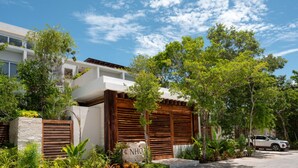 A modern house with a white exterior, wooden shutters, and a stone foundation. - NHOA 107A Lux 2BR Condo Pool access in Aldea Zama (Tulum)
