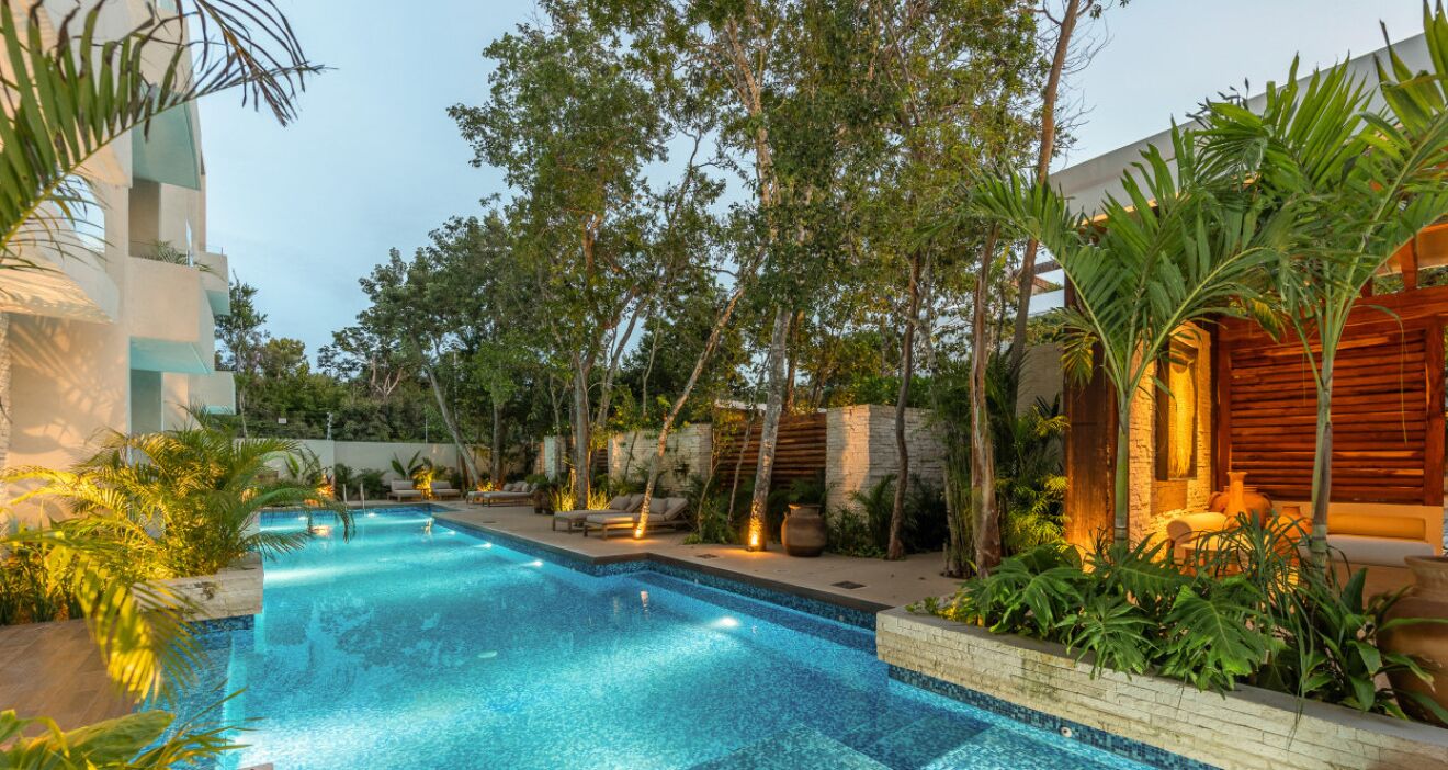 A swimming pool with a tiled edge, surrounded by lush greenery and a wooden structure.