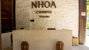 Ein Empfangsschalter mit einem Schild, auf dem 'NHOA CONDOS TULUM' steht, und je eine hölzerne Maske auf beiden Seiten.