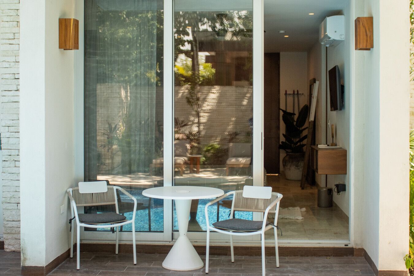 A glass door leading to a patio with a round table and two chairs, a small potted plant, and a TV mounted on the wall.