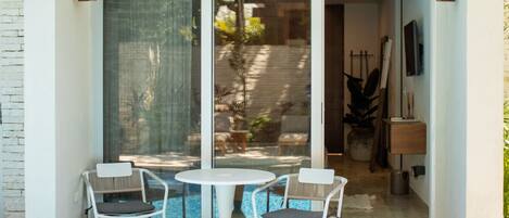 A glass door leading to a patio with a round table and two chairs, a small potted plant, and a TV mounted on the wall.