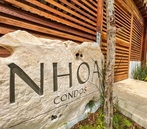 A stone sign with "NHOA CONDOS" for a residential property. - NHOA 107B Lux 1BR Condo Pool access in Aldea Zama (Tulum)