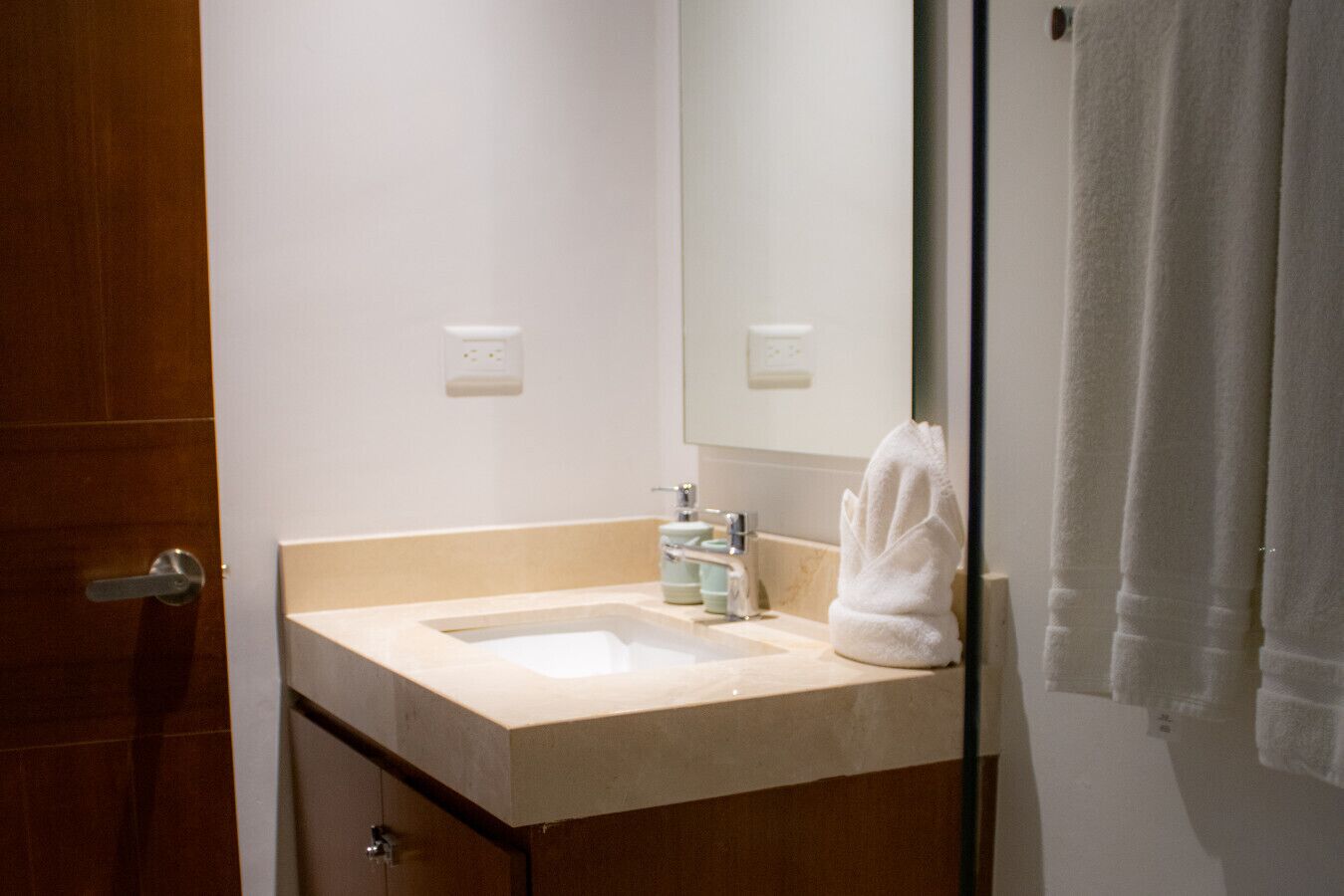 A bathroom with a sink, mirror, towel, and a door.
