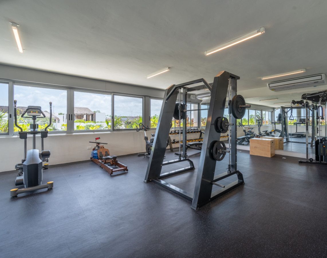 Ein Fitnessstudio mit unterschiedlichen Trainingsgeräten, großen Fenstern und Blick auf Grünflächen.