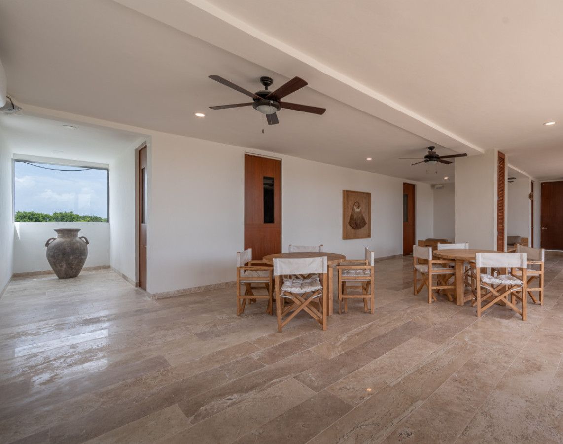 A spacious room with a large dining table and chairs, a ceiling fan, and a view of the outdoors.