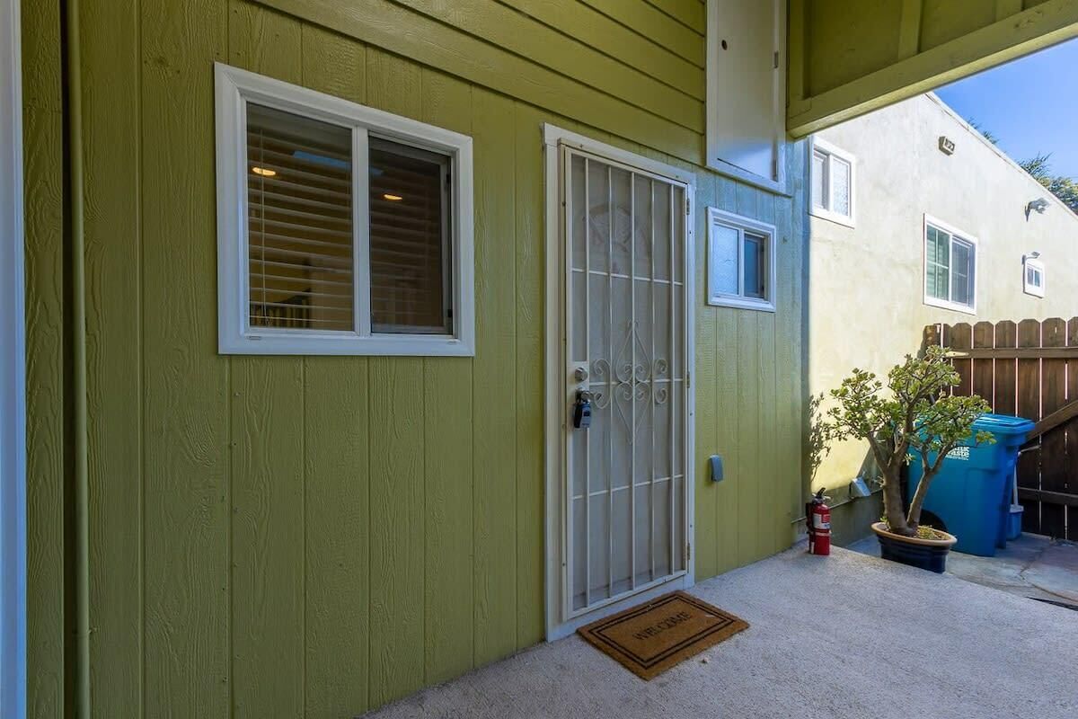 Une maison verte avec une porte blanche, une fenêtre et un petit arbre dans un pot.
