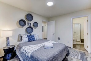 A neatly arranged bedroom with a large bed, a bedside table, a wall-mounted lamp, and a door leading to a bathroom. - @ Marbella Lane - Bright and Cozy Home Near SFO (San Mateo)