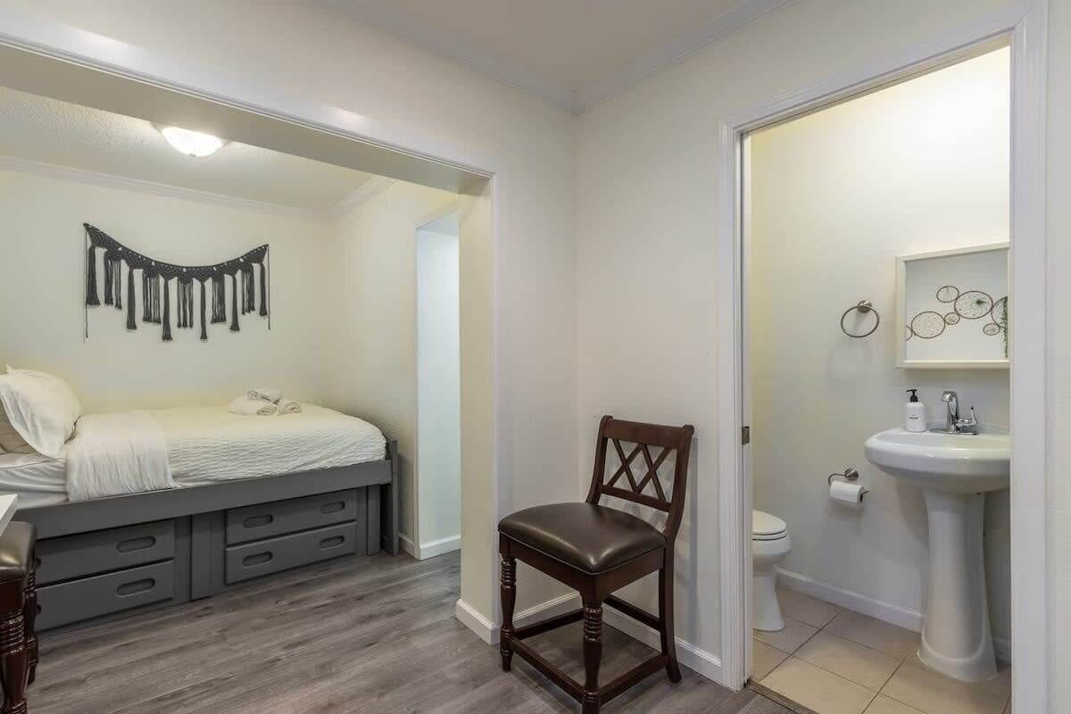 Quarto com cama, cadeira, mesa de cabeceira e banheiro com pia e vaso sanitário.