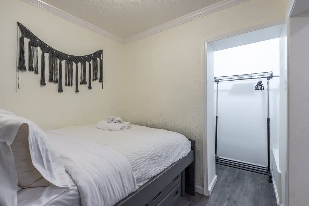 A bedroom with a bed, a wall-mounted macrame piece, and a door leading to a bathroom.