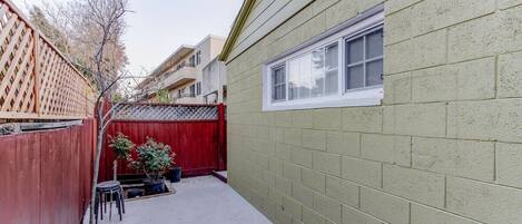 A narrow backyard with a red fence, a small patio area, and a window on a brick wall.