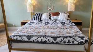 Een hemelbed met een beddengoed met een patroon, twee bedlampjes en een dromenvanger aan de muur.