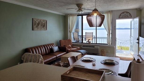 Een gezellige woonkamer met een bruine leren bank, een eettafel gedekt met borden, en uitzicht op de zee door grote ramen.
