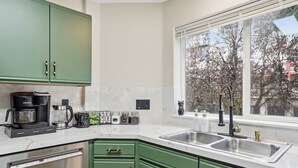Eine moderne Küche mit grünen Schränken, einem eingebauten Geschirrspüler, einer Kaffeemaschine und einem Fenster mit Blick auf Bäume.