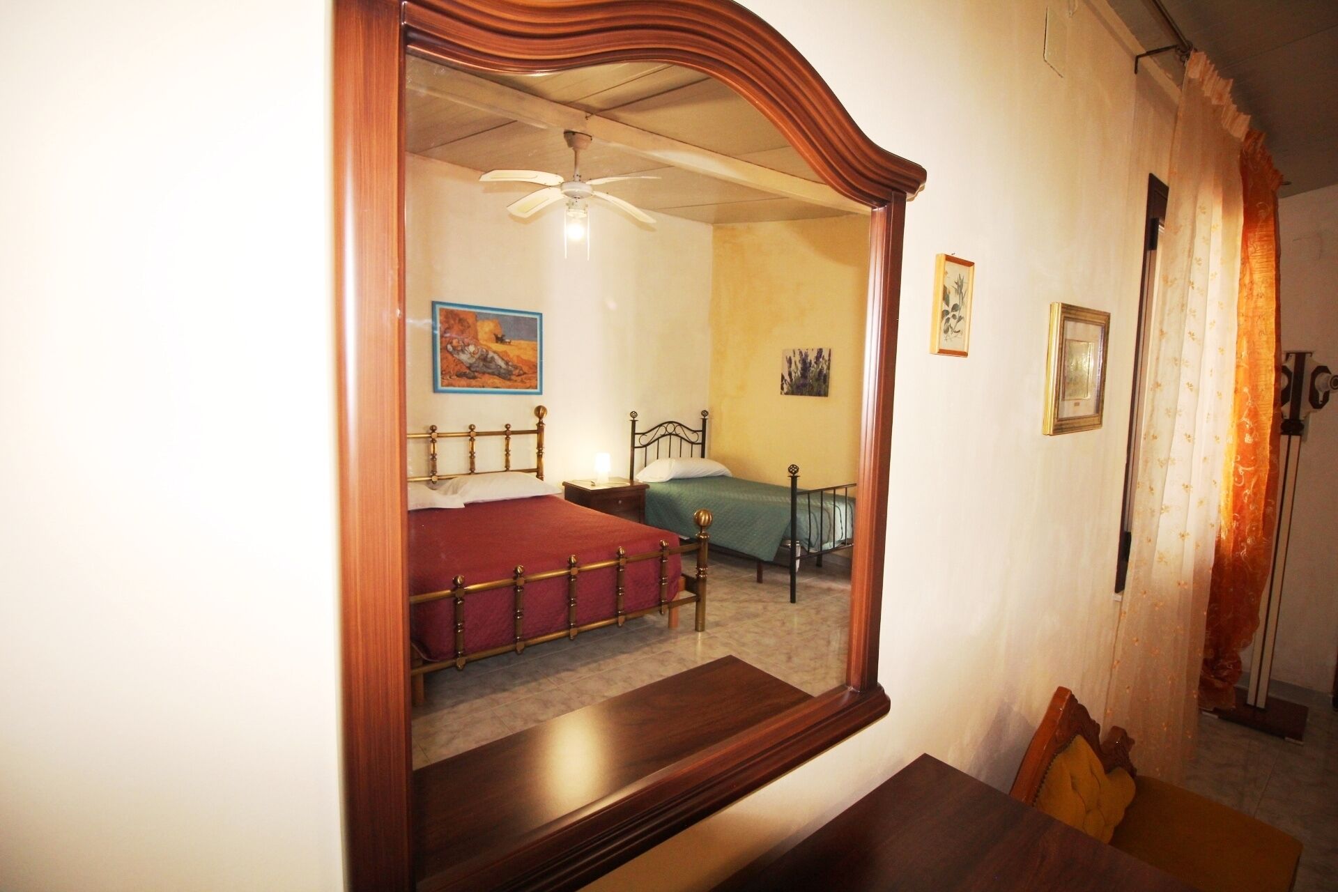 A bedroom with two beds, a ceiling fan, and a large mirror.