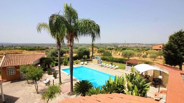 A swimming pool with lounge chairs, surrounded by palm trees and a view of a distant landscape. - VILLA VENERA - Amazing Holiday House (Solarino)