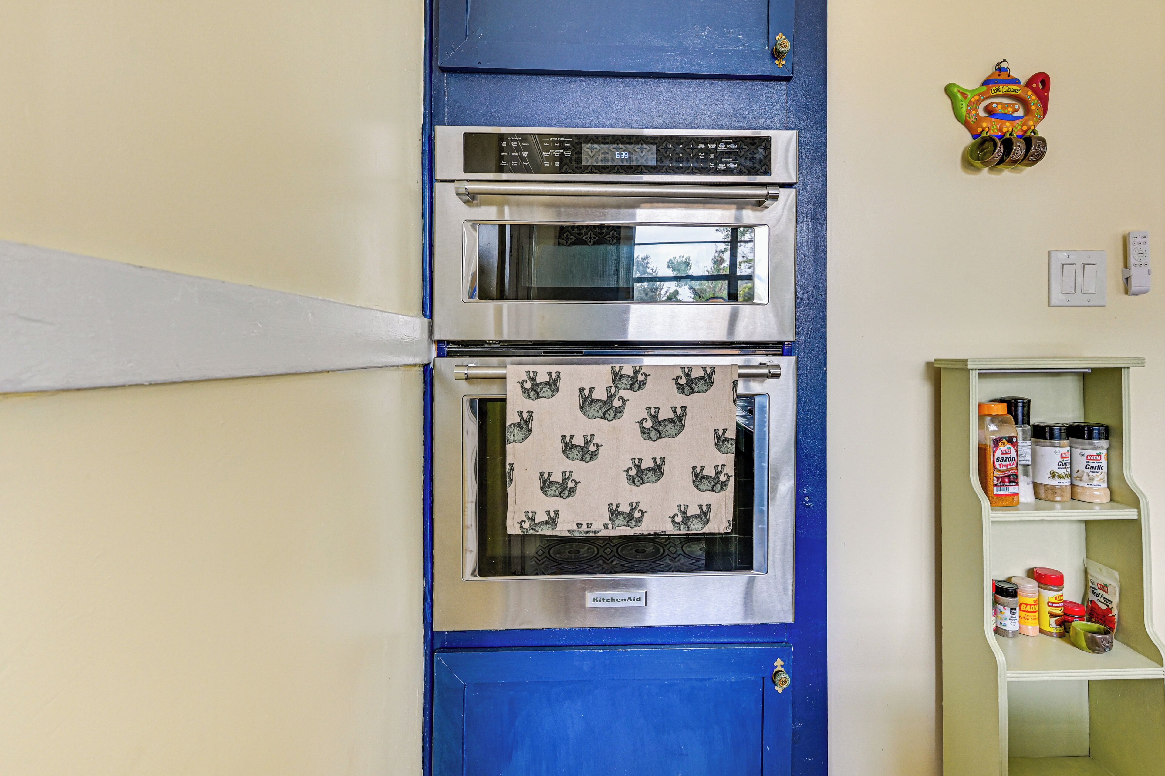 A kitchen with a double oven, a shelf with spices, and a wall-mounted light switch.