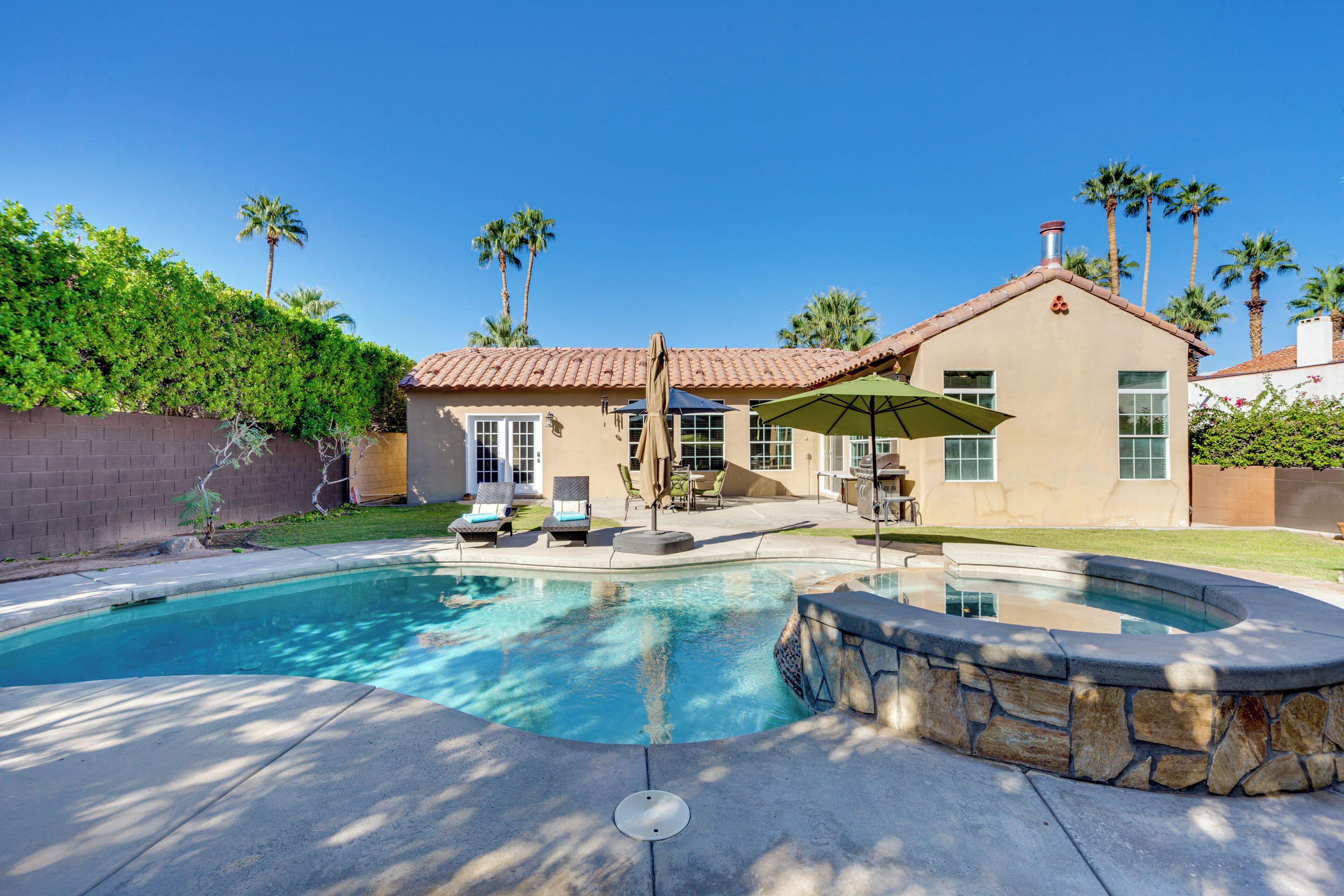 A house with a swimming pool, patio furniture, and palm trees.