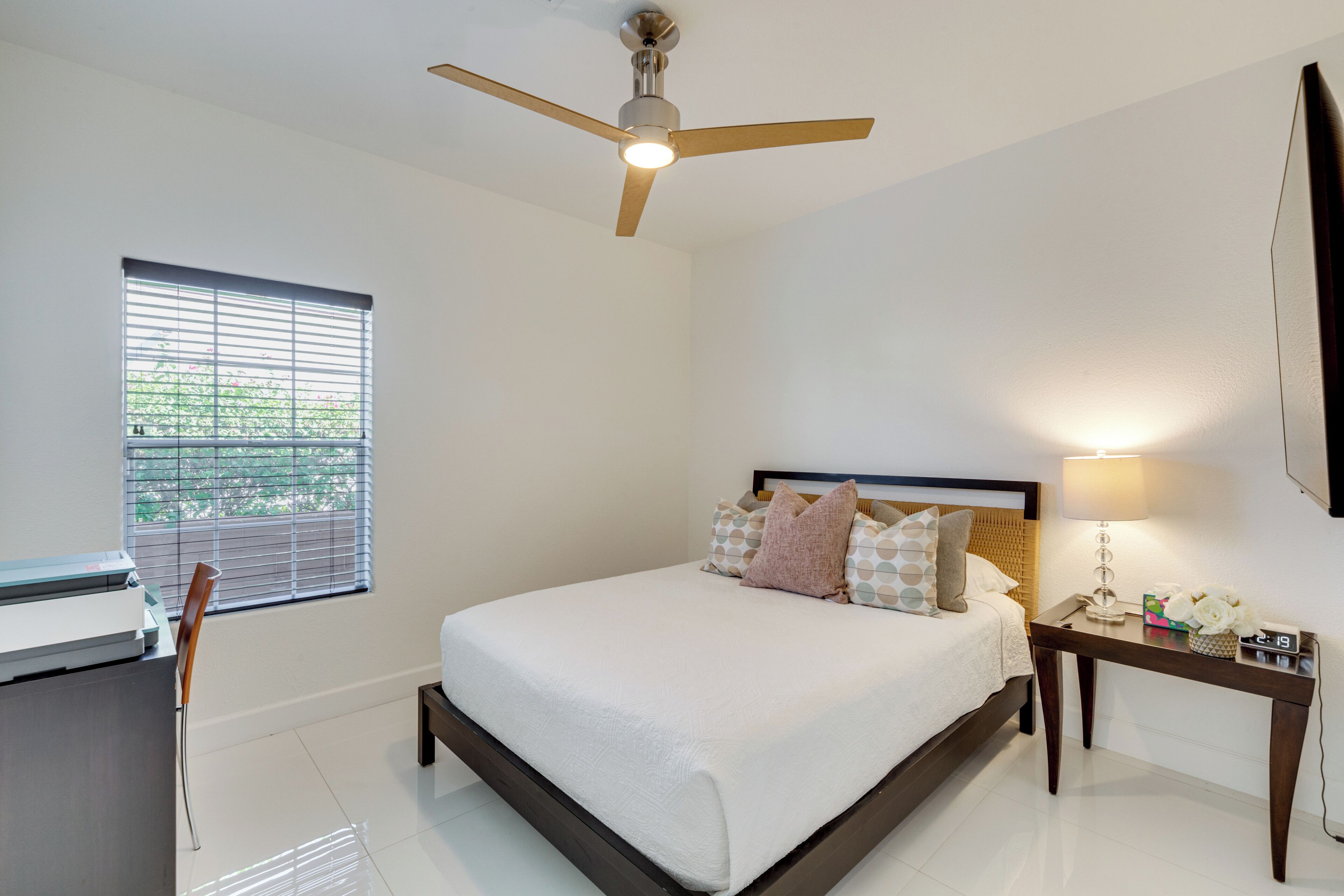 A neatly arranged bedroom with a bed, bedside table, lamp, and a ceiling fan.