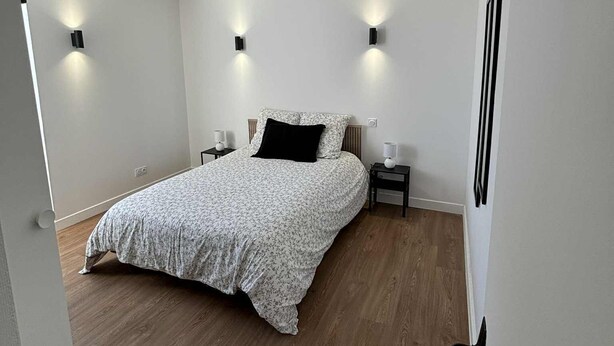 A bedroom with a bed, bedside tables, and wall-mounted lighting. - Modern apartment in the heart of the Auvergne. 10 min from Les Termes de Châtel-Guyon. (Combronde)