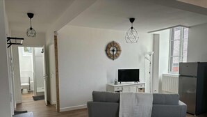 A modern living room with a grey sofa, a flat-screen TV on a white cabinet, and a wooden-framed clock on the wall. - Modern apartment in the heart of the Auvergne. 10 min from Les Termes de Châtel-Guyon. (Combronde)