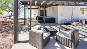 Un patio al aire libre con muebles de mimbre, una zona de estar techada y una piscina al fondo.