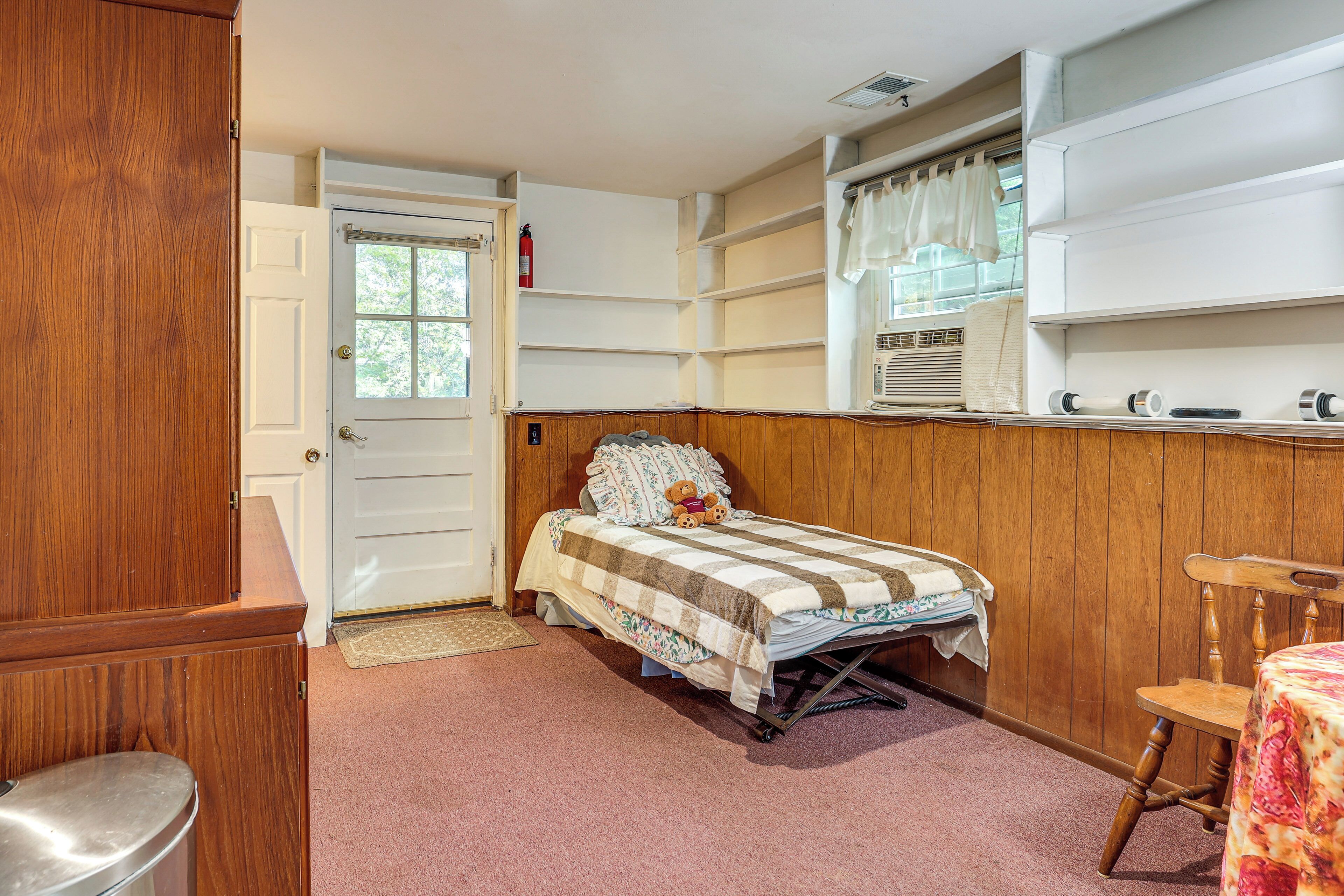 A bedroom with a wooden headboard, a bed with a floral bedspread, a window with curtains, and a wooden chair.