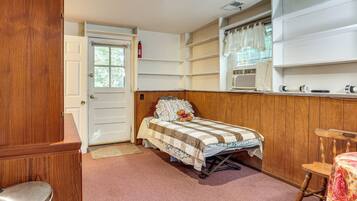 A bedroom with a wooden headboard, a bed with a floral bedspread, a window with curtains, and a wooden chair.