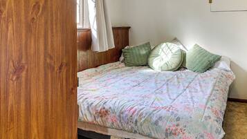 A bedroom with a wooden wardrobe, a bed with floral bedding, and a window with curtains.