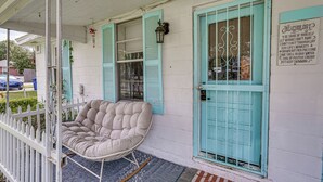 A porch with a cushioned chair, a teal door, and a sign with motivational text. - Little Cove Cottage! Walk to Dtwn Panama City (Panama City)
