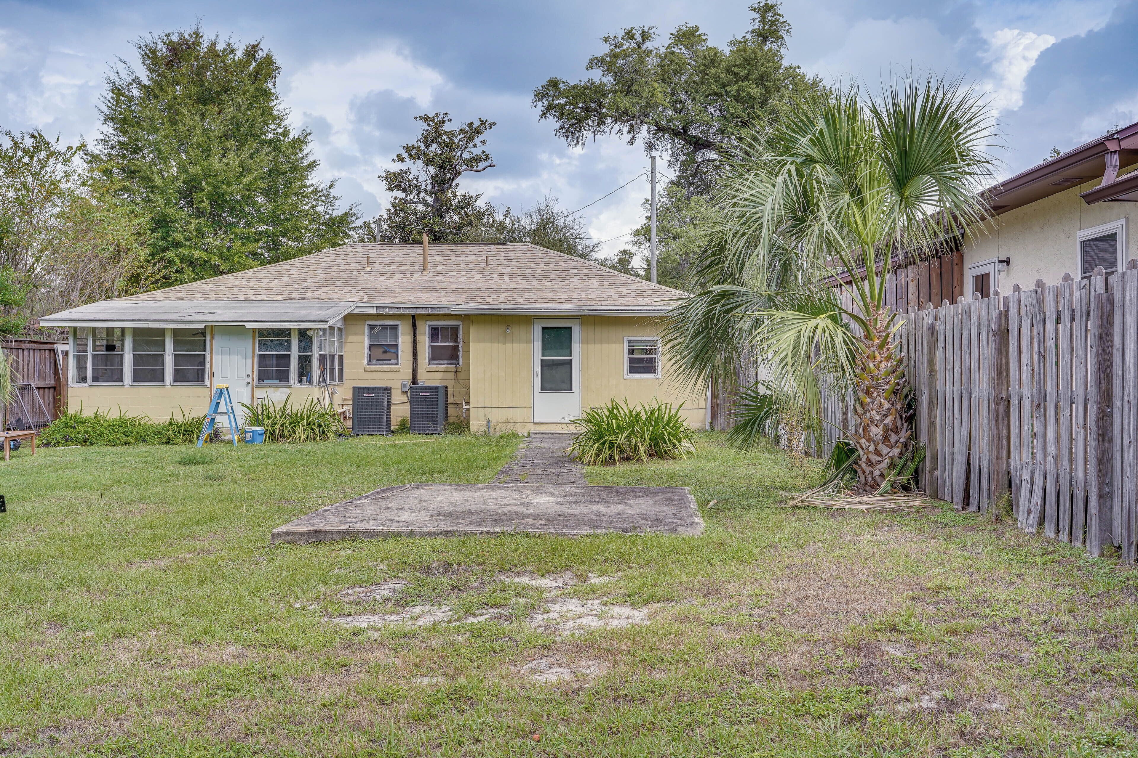 A single-story house with a front yard, a wooden fence, and a palm tree.