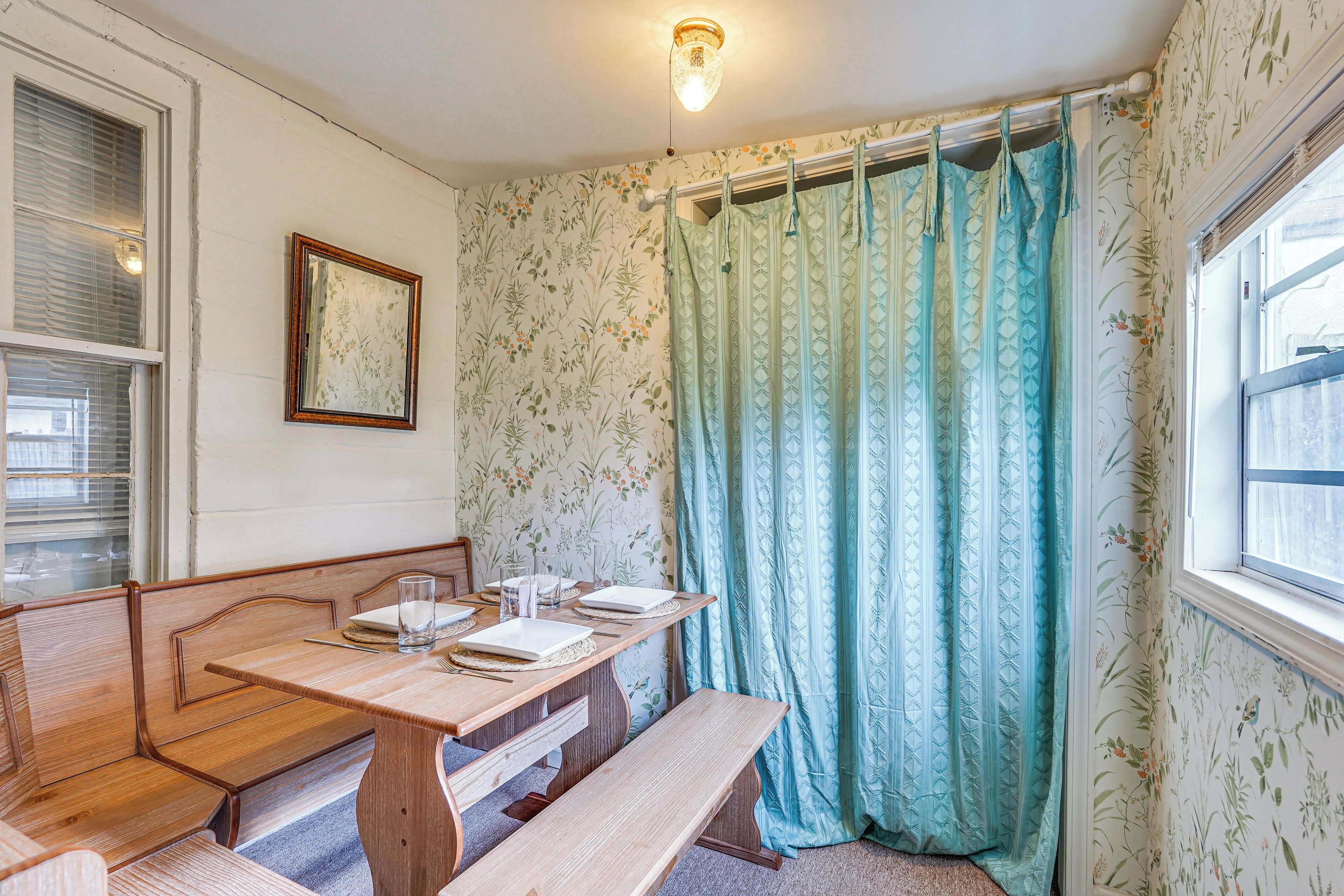 Un área de comedor con una mesa de madera y bancos, un cuadro en la pared y una ventana con cortina.
